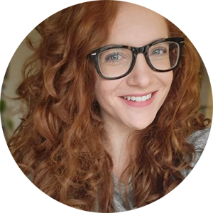 Image description: Kolo, a white woman with glasses, ginger curly hair, smiling at the camera.