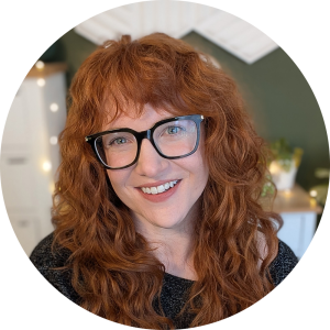 Headshot of HelloItsKolo, AKA Kolo Jones. She is a white woman with long curly ginger hair and thick framed glasses. she smiles at the camera.